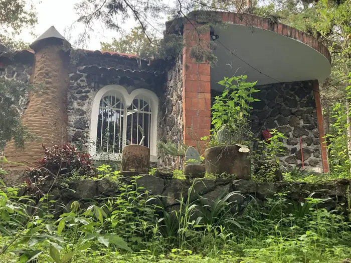 A stone building with tall arched windows and a brick column, framed by greenery.