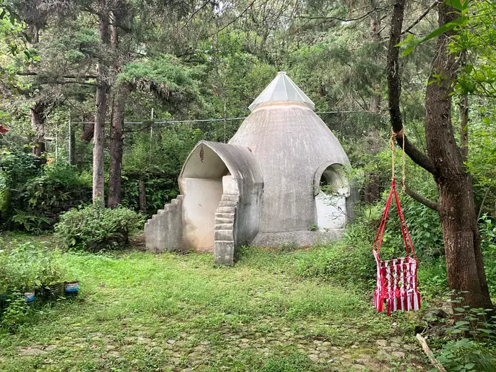 A rendered dome structure on a lawn among pines, with a hanging chair nearby.